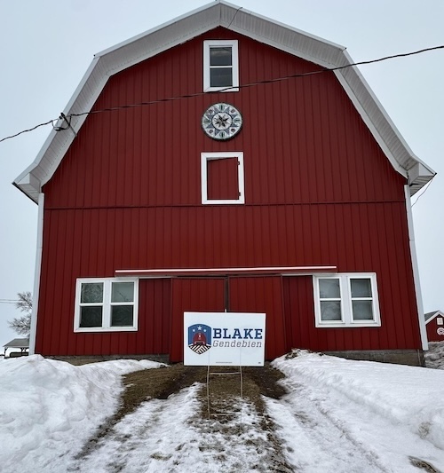 A Blake Gendebien yard sign in front of a red barn.