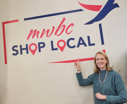 Photo of Brooke in front of a wall that says "MWBC Shop Local"