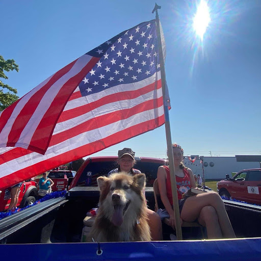 Callie's daughters and dog sitting in bed  of truck with an American flag