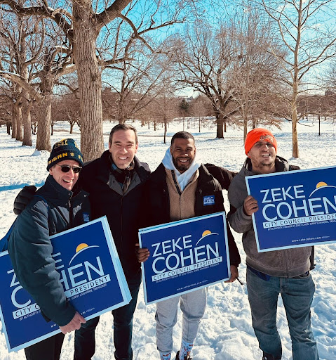 Zeke and members of the team holding yard signs in the snow.
